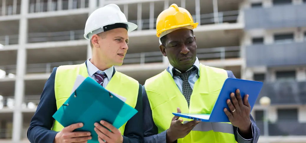 Two architects in warnvests, standing on a building and discussing a construction project
